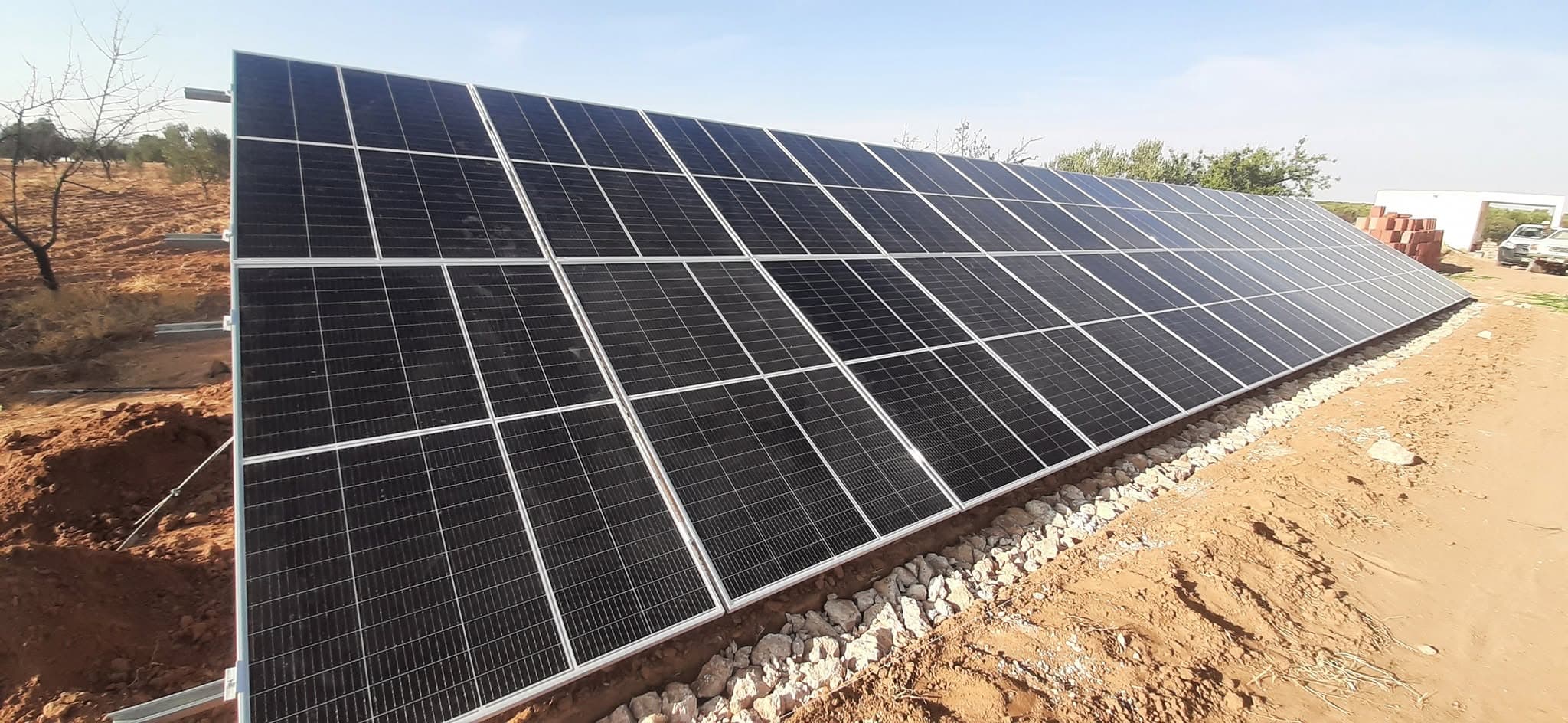 Grande installation de panneaux solaires photovoltaïques sur un terrain sec et rocailleux ensoleillé.