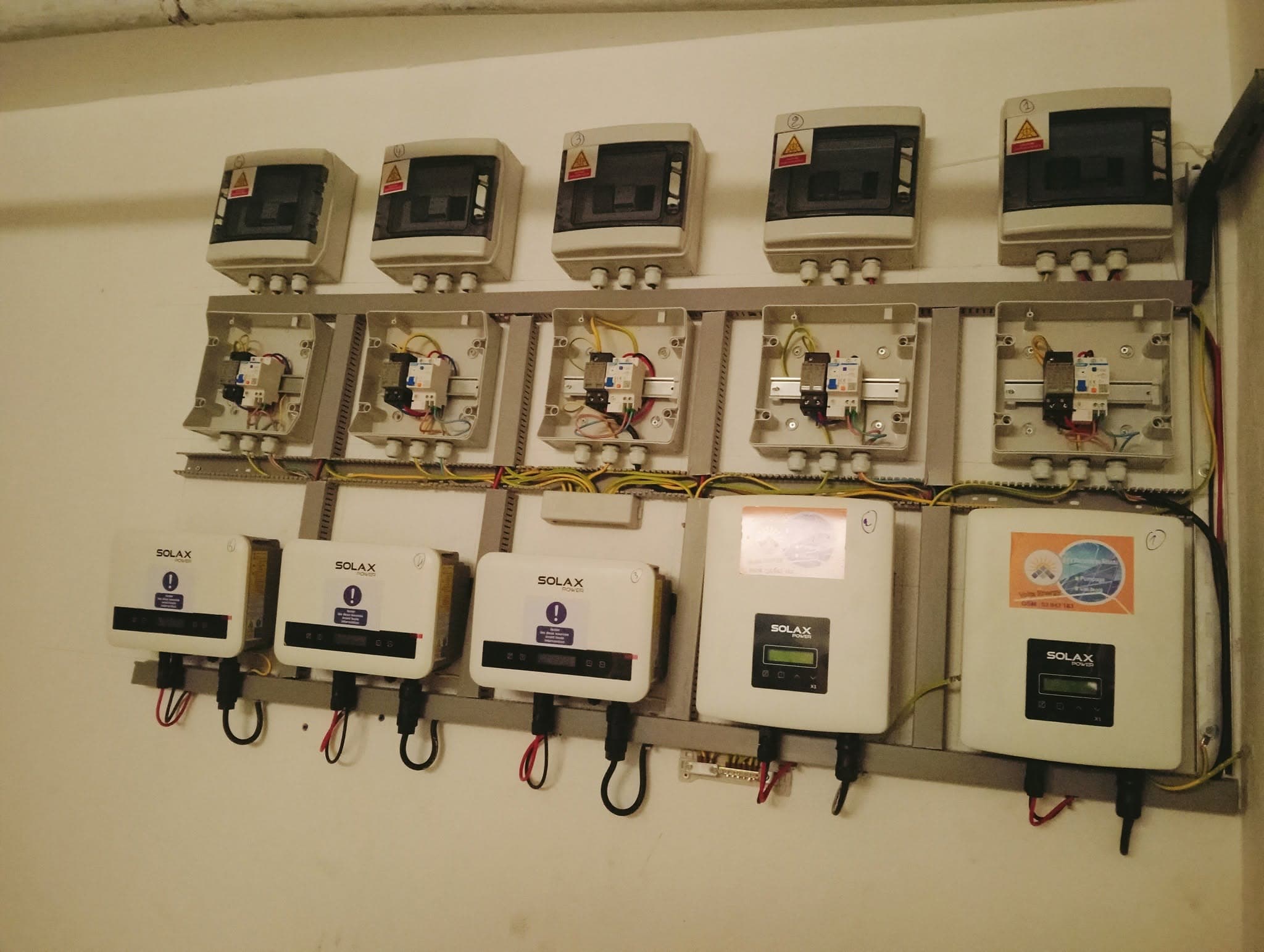 Installation murale d'onduleurs Solax Power et de boîtiers de disjoncteurs avec câblage électrique apparent.