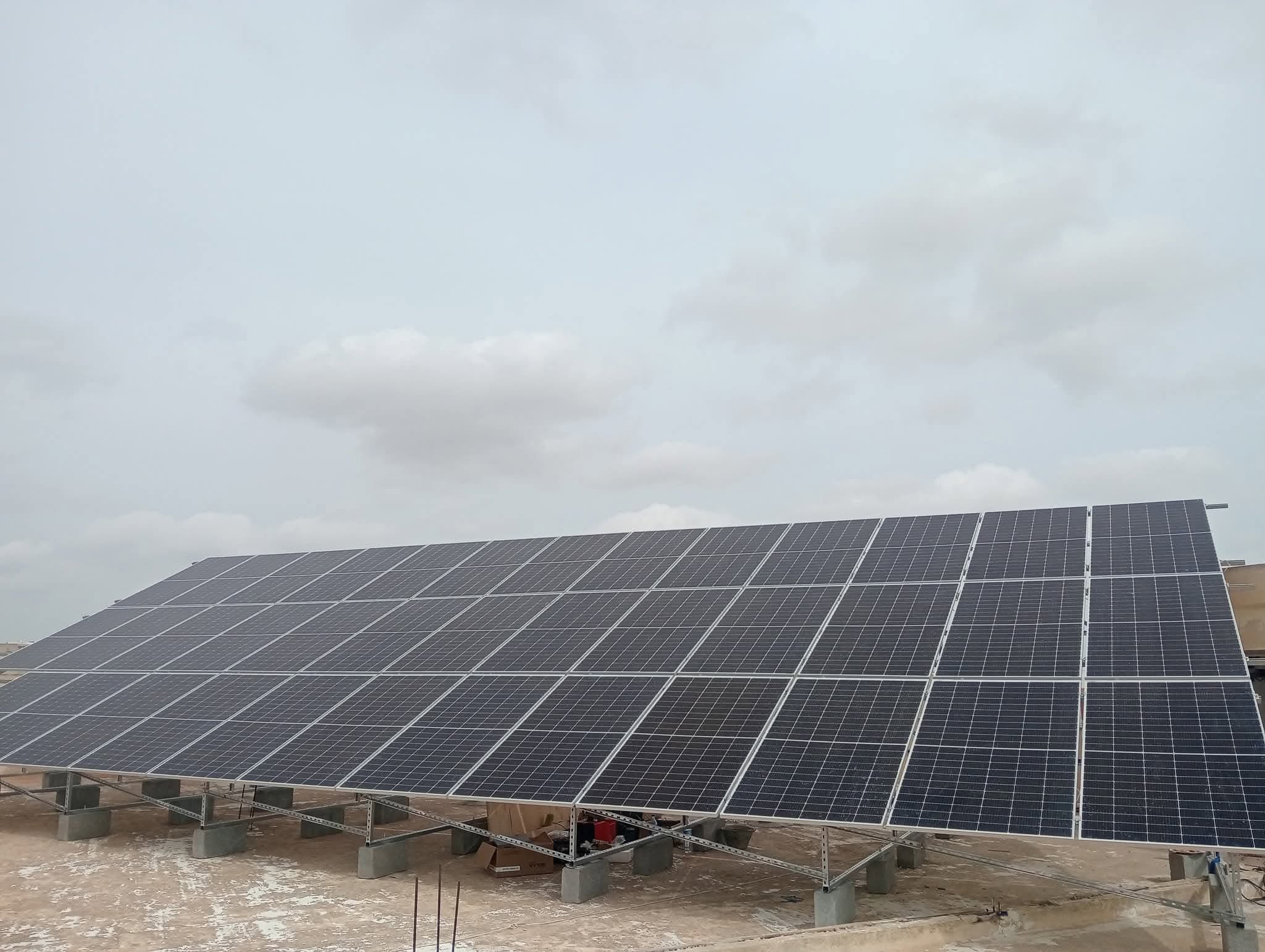 Large réseau de panneaux solaires installés sur un toit plat sous un ciel nuageux.