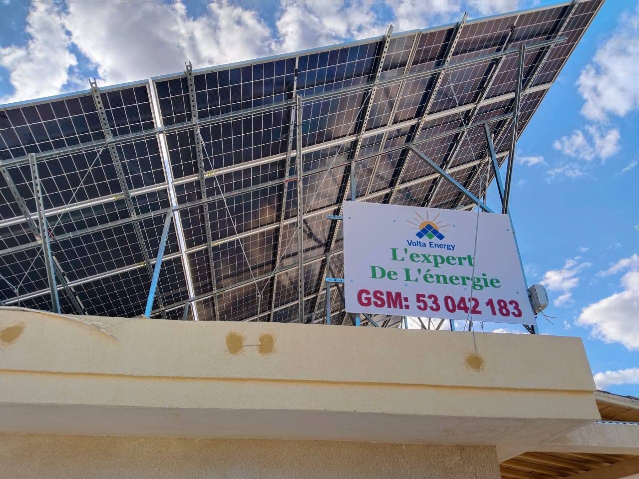 Panneaux solaires sur structure métallique avec enseigne Volta Energy sous un ciel bleu et nuageux.